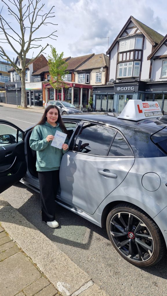 Pass Wheels pupil holding their practical driving test pass certificate beside the school car