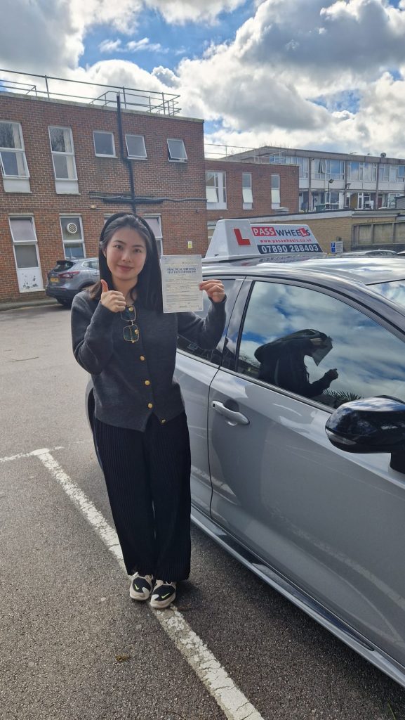 Pass Wheels pupil holding their practical driving test pass certificate beside the school car