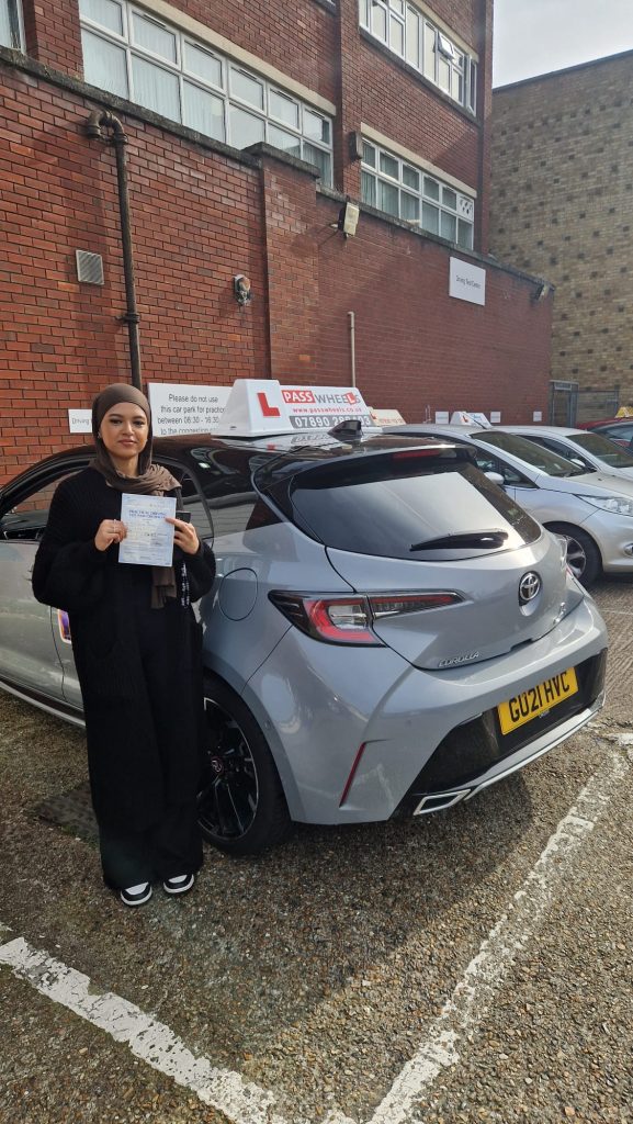 Pass Wheels pupil holding their practical driving test pass certificate beside the school car